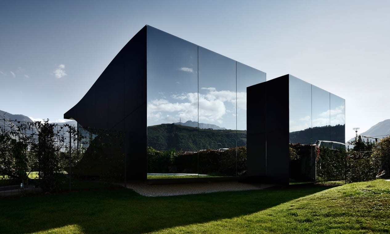 A building with mirrored walls reflecting the grass and hills surrounding it making it appear almost camouflaged