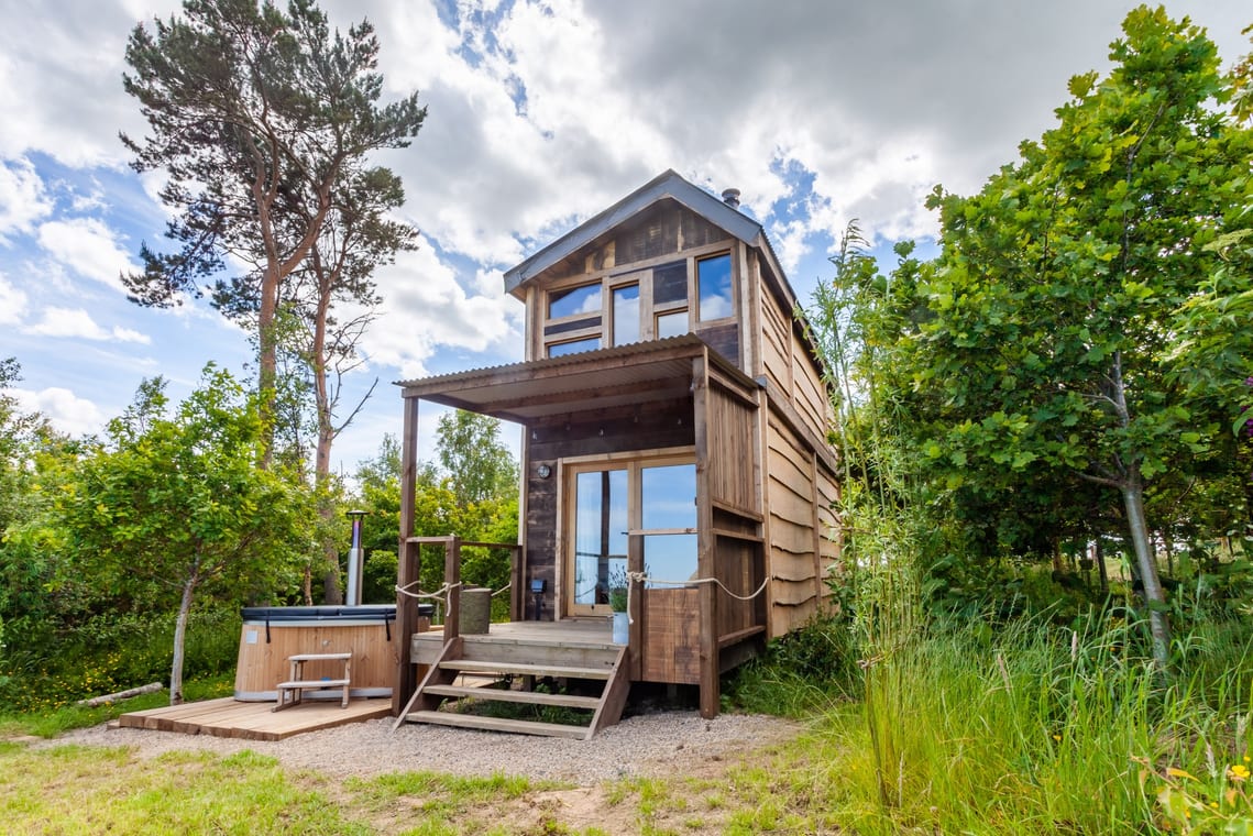 Two storied wooden lodge with a wooden deck with steps down to ground level at the front and a hot tub outside the front of it