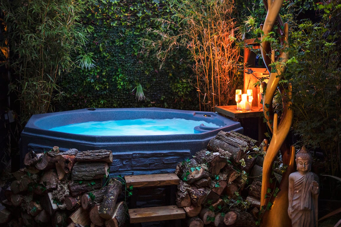 Hot tub set up with wooden steps up into it and candles and two glasses of fizz on a side table