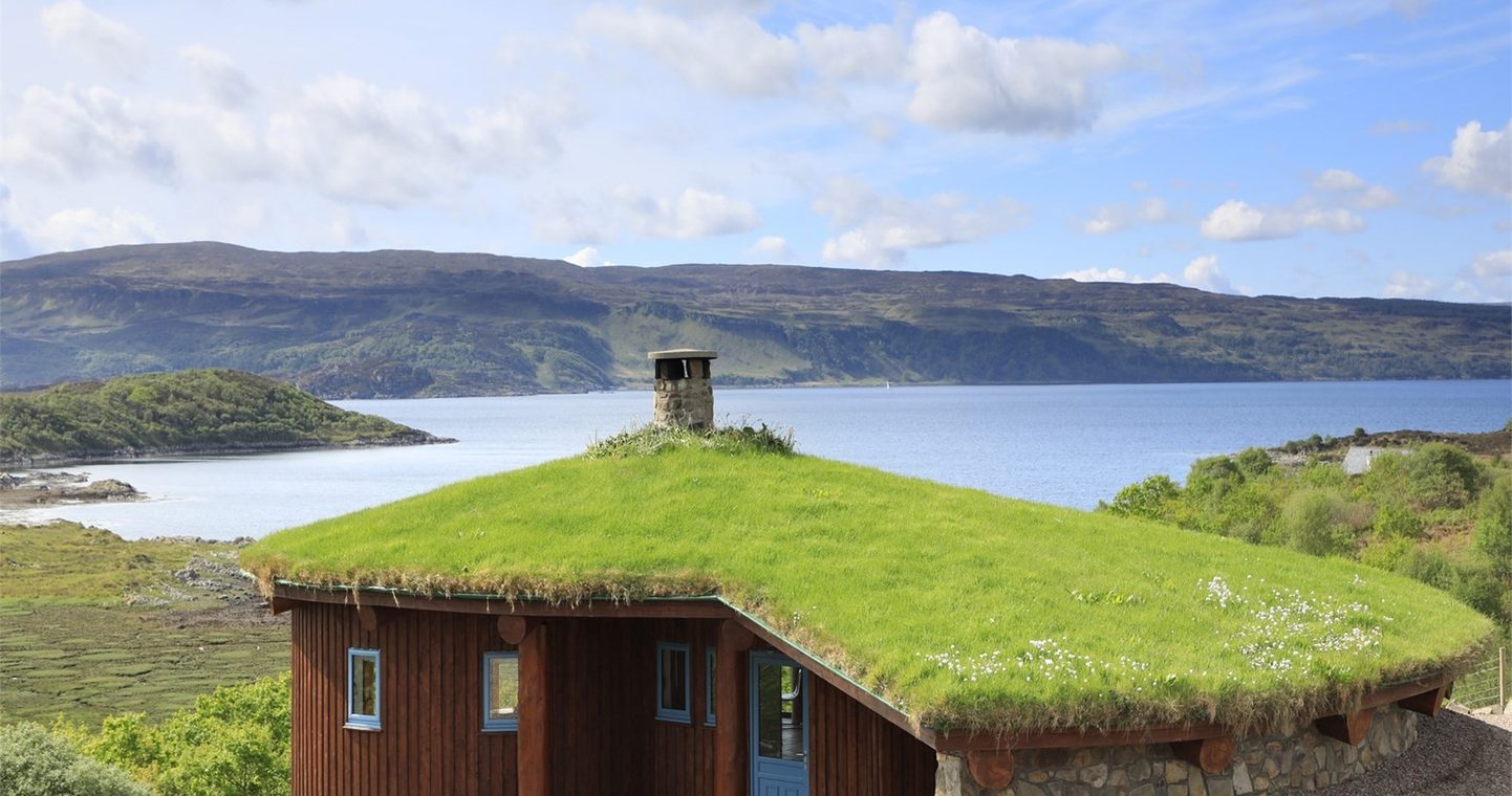 Cottage with a turfed roof and wooden panels on the outer walls next to a Loch