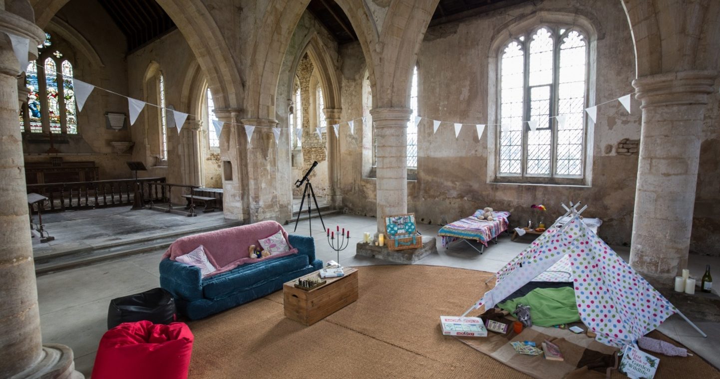 Sofa and beans bags with cushions, toy tipi tent and one camp bed set up inside a Church
