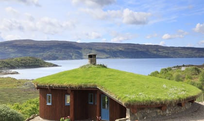 Cottage with a turfed roof and wooden panels on the outer walls next to a Loch