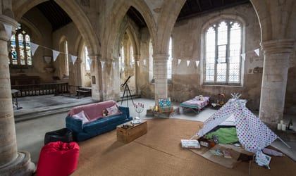 Sofa and beans bags with cushions, toy tipi tent and one camp bed set up inside a Church