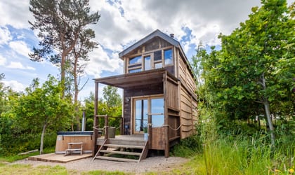 Two storied wooden lodge with a wooden deck with steps down to ground level at the front and a hot tub outside the front of it