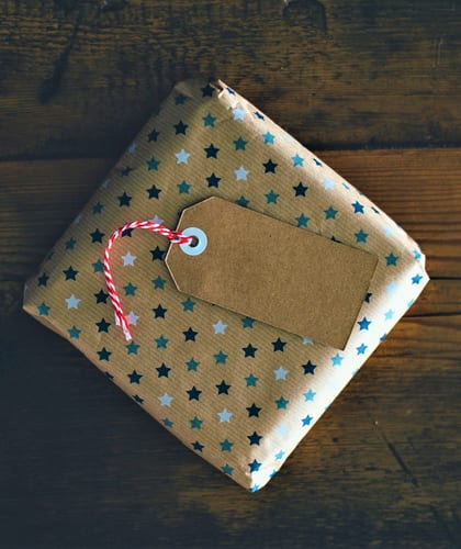 Small parcel wrapped in brown paper with a pattern of coloured stars and a gift label attached