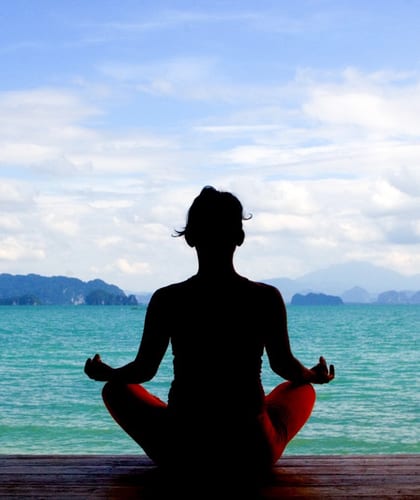 Person sat cross legged doing yoga in front of a turquoise ocean