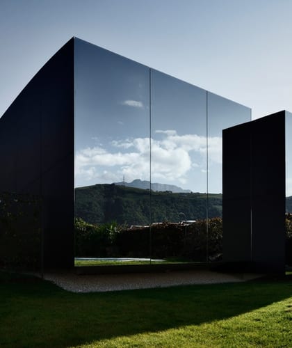 A building with mirrored walls reflecting the grass and hills surrounding it making it appear almost camouflaged