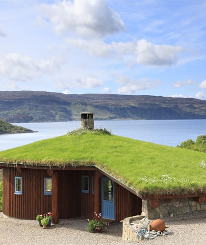 Cottage with a turfed roof and wooden panels on the outer walls next to a Loch