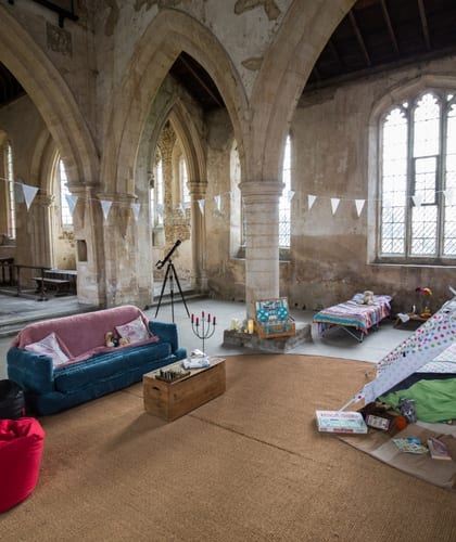 Sofa and beans bags with cushions, toy tipi tent and one camp bed set up inside a Church