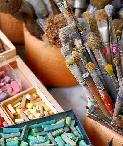 Pots of pencils, boxes of coloured chalks and pots of paint brushes