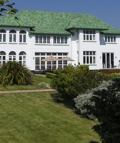 A large white house with green roof tiles and a large lawn in front of it