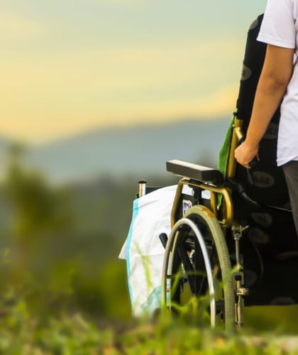 The back of a person holding the handles a wheelchair ready to push it