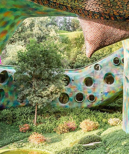 A large abstract looking sculpture built into grassy banks with circular windows and multicolour outer walls
