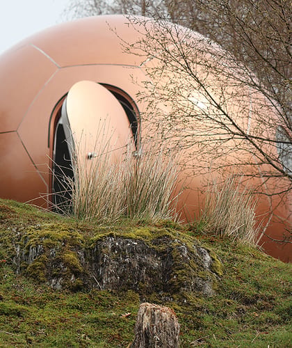 Copper colour, metallic glamping pod on grassy mossy ground