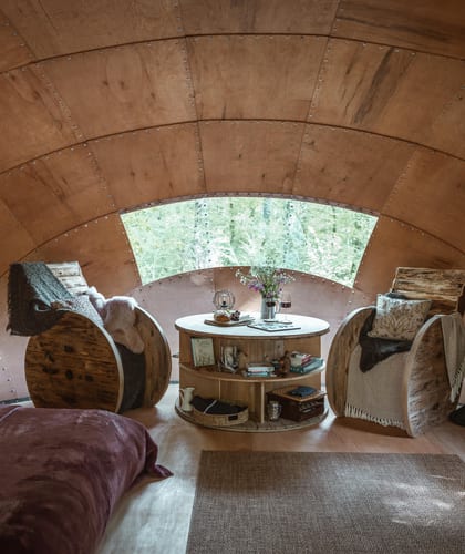 Double bed, two chairs and a table inside a dome-shaped wooden retreat