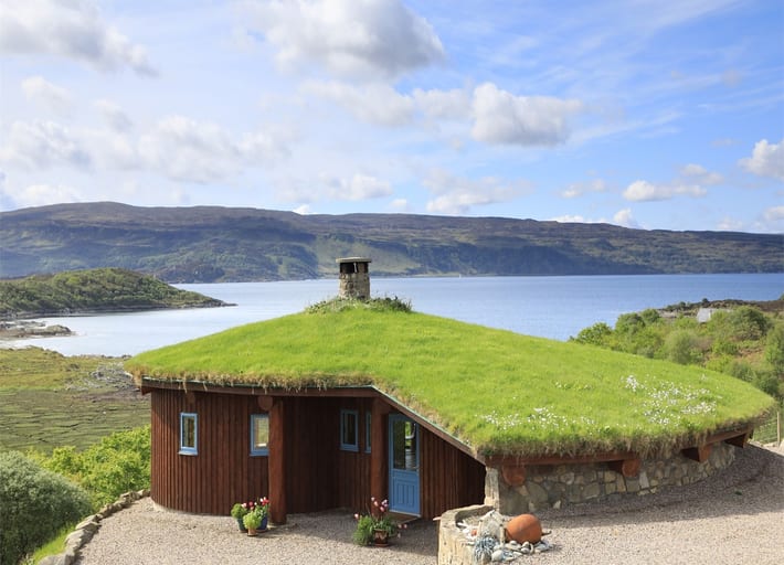 Cottage with a turfed roof and wooden panels on the outer walls next to a Loch