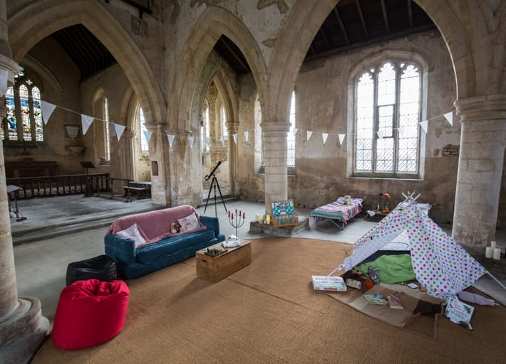 Sofa and beans bags with cushions, toy tipi tent and one camp bed set up inside a Church